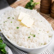 A serving bowl of crockpot rice topped with two pats of butter.