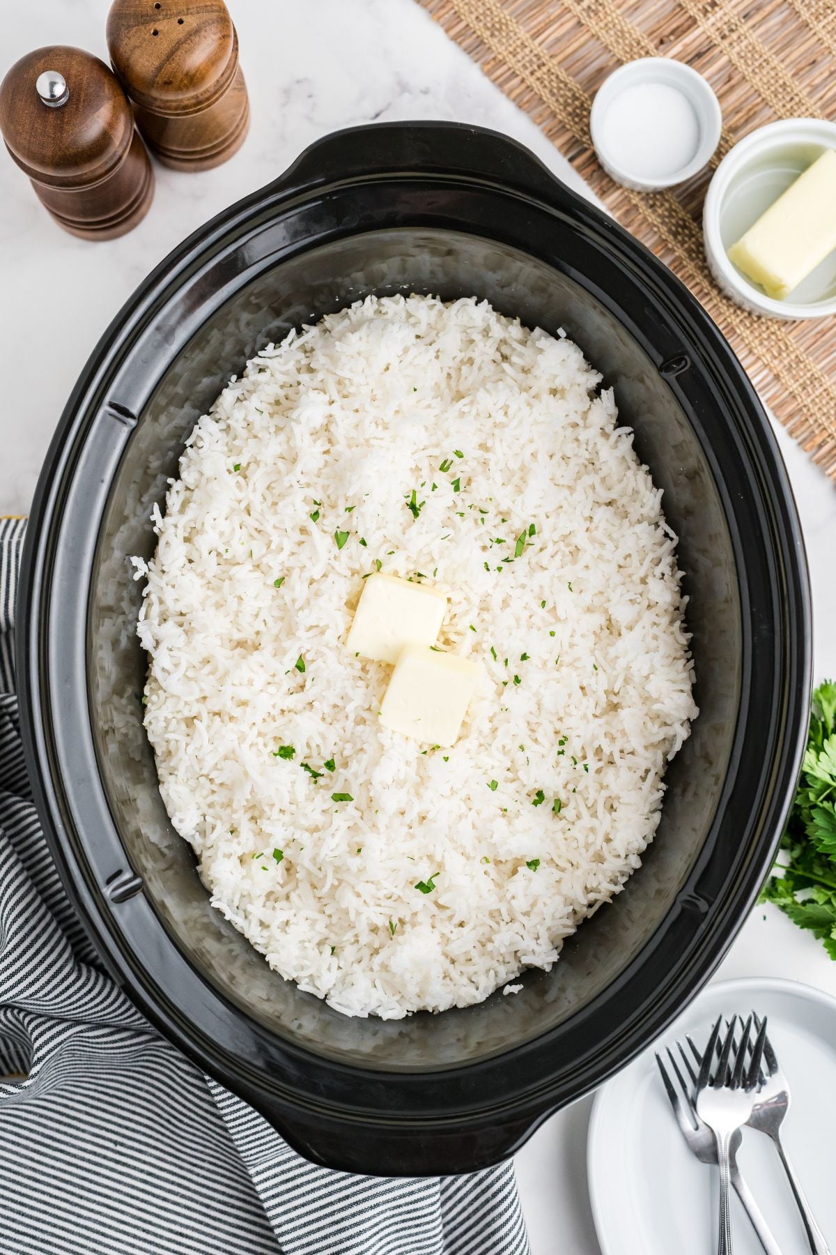 Crock pot with rice garnished with parsley and butter on top.