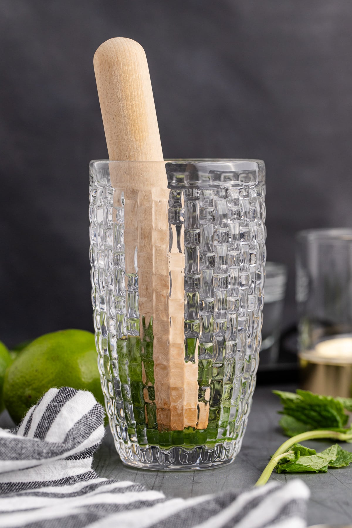 cucumber and a few mint leaves being muddled in a cocktail shaker