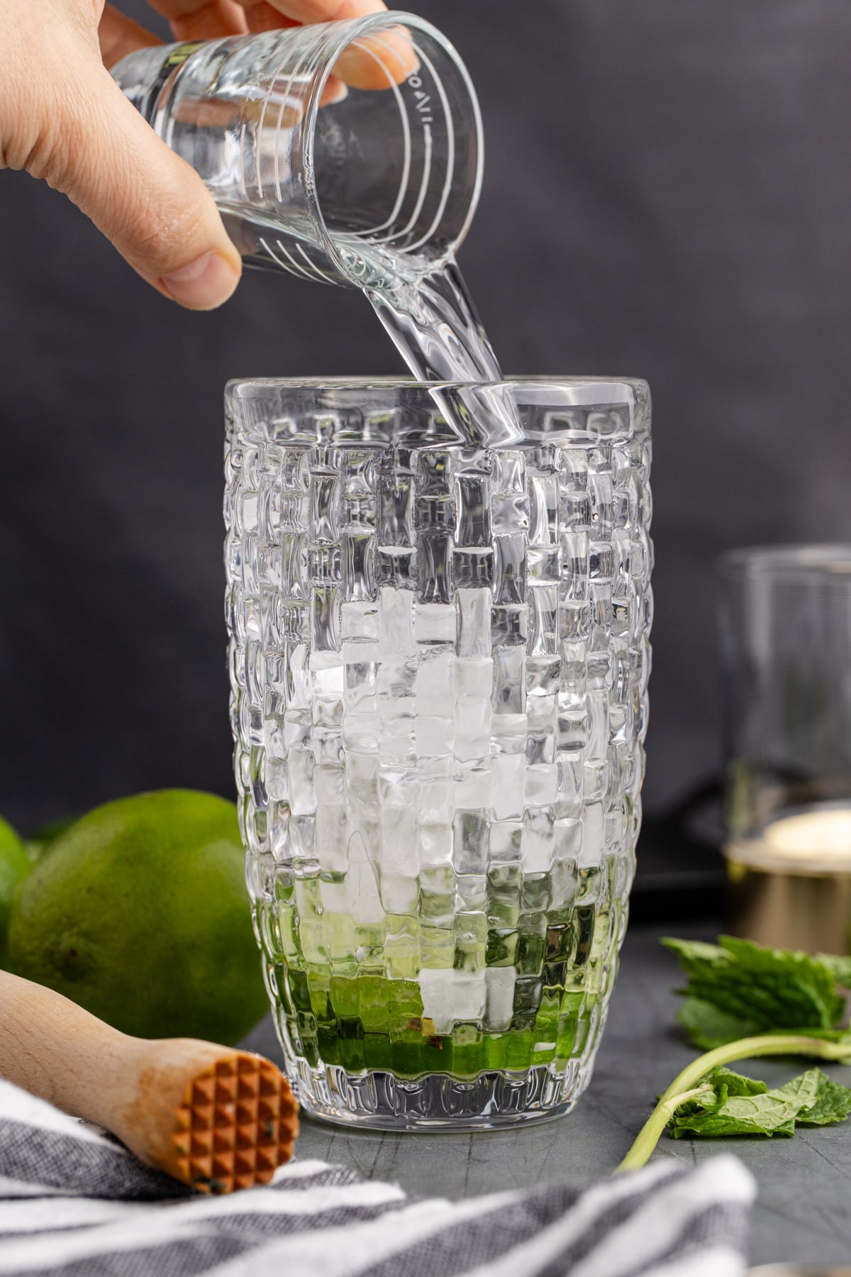 Gin being added to cocktail shaker with ice, lime juice and simple syrup.
