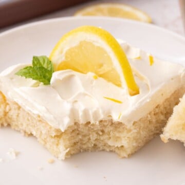 A slice of lemon sheet cake on a plate garnished with a lemon slice and mint.