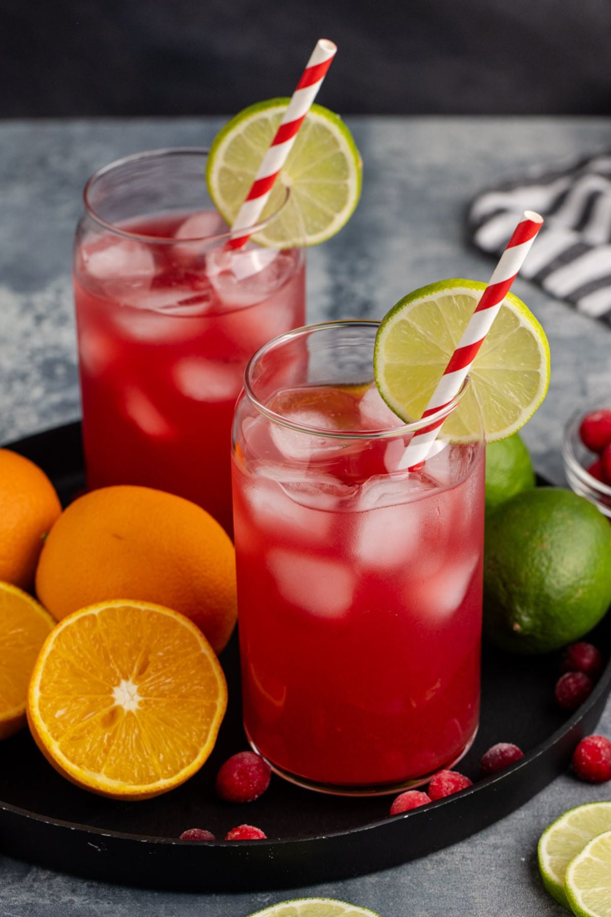 two cocktails on a tray with oranges and limes
