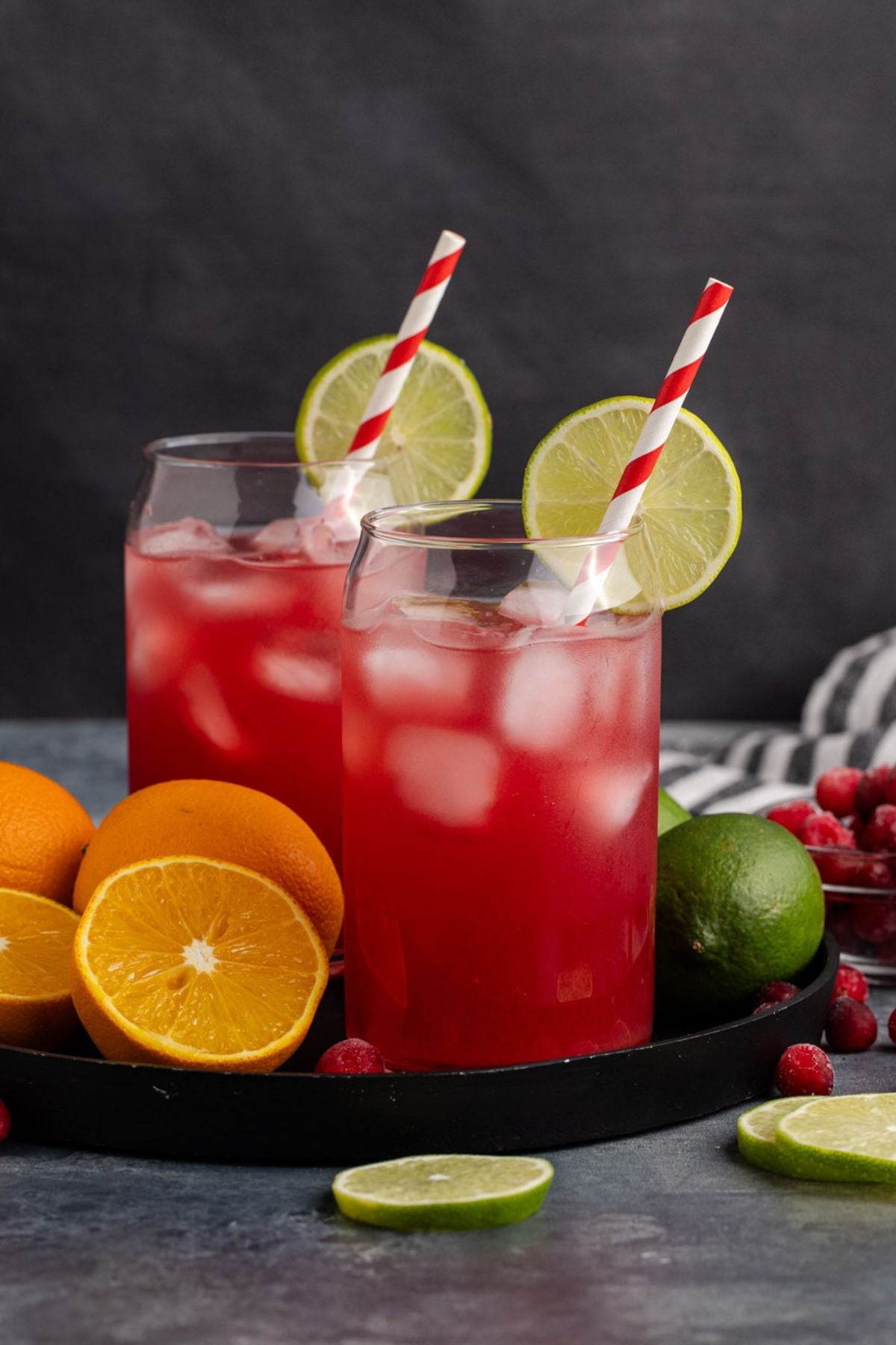 two garnished drinks on a tray with oranges and limes