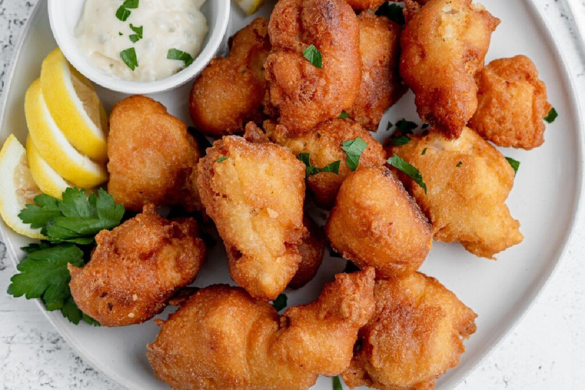 A plate full of fish nuggets with dip and lemon slices.
