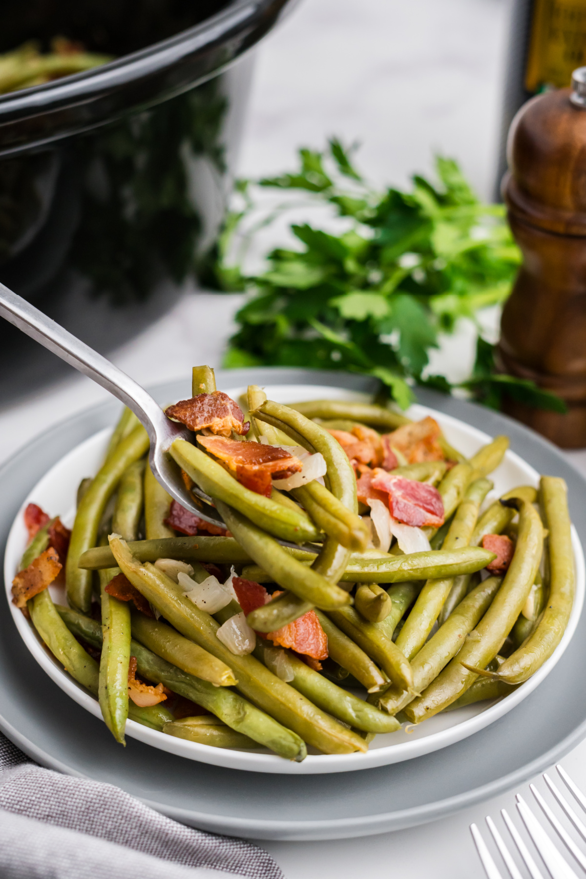 Bacon, green beans and onions on a plate with a bite of food on a fork.