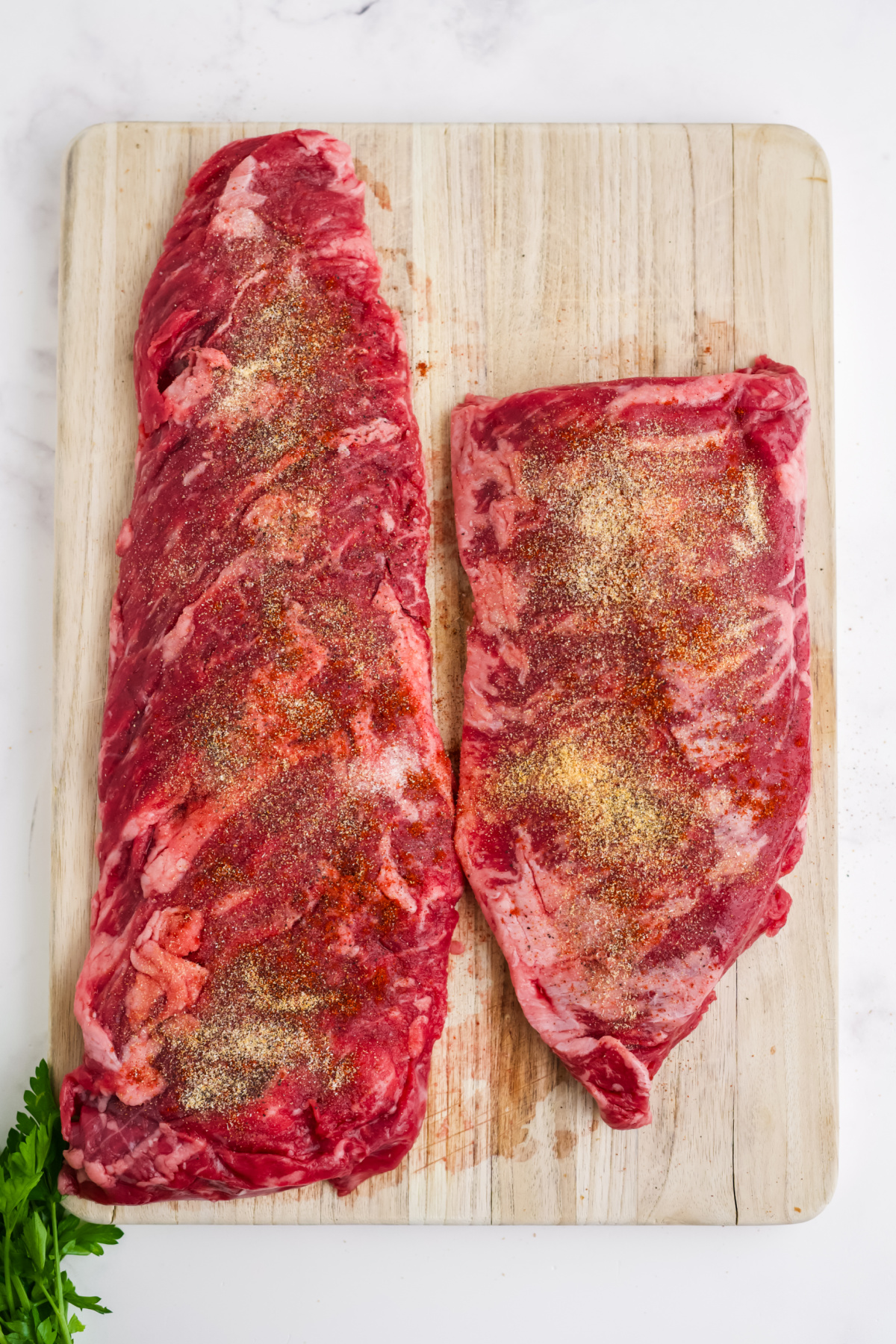 Skirt steak on a cutting board and seasoned with spices.