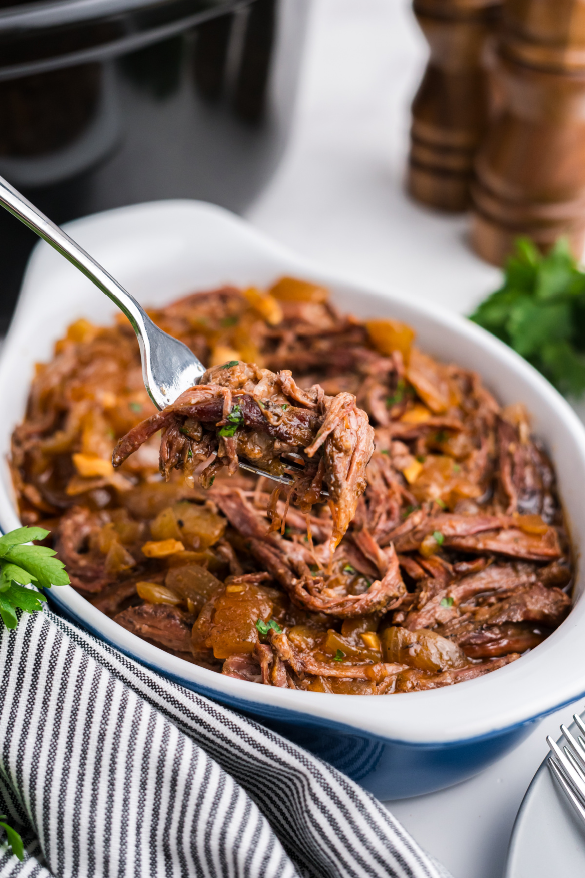 A fork full of shredded skirt steak held up in the air over a dish of more.