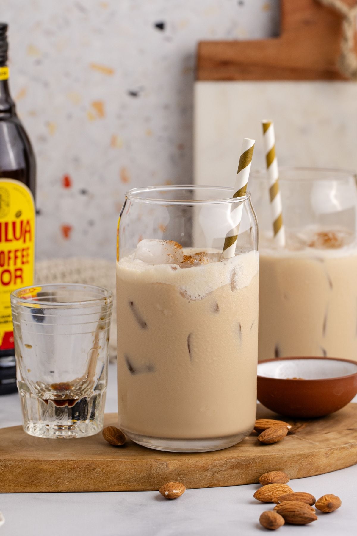 Two drinks on a cutting board with a shot glass and bottle of kahlua.
