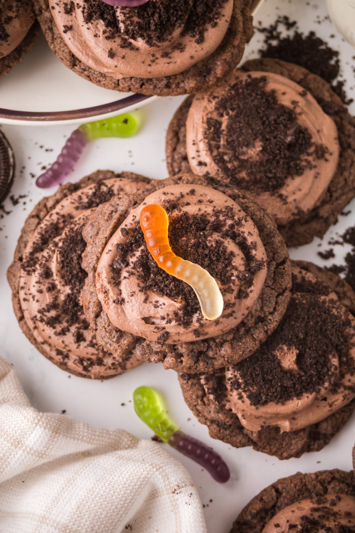 Multiple dirt cake cookies stacked on a table with a gummy worm in the center.