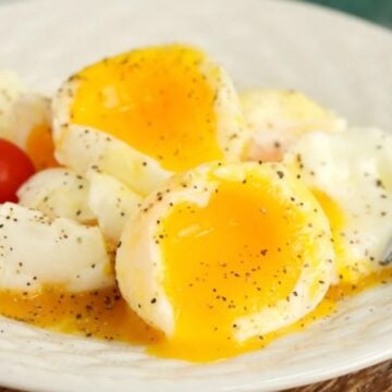 A plate with two eggs, their yolks broken and runny, seasoned with pepper.