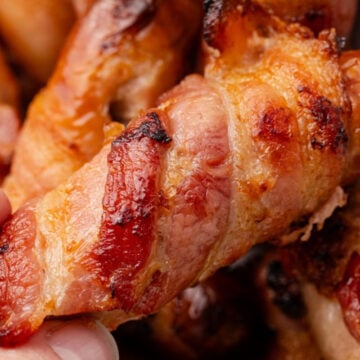 A bacon wrapped sausage lifted from a pile.