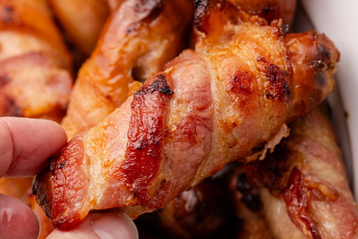 A bacon wrapped sausage lifted from a pile.