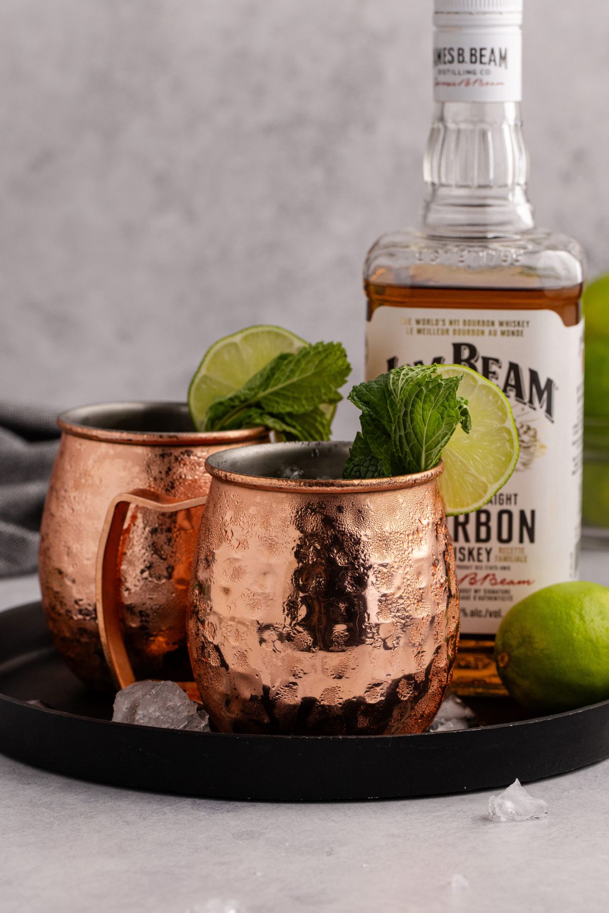 Two garnished drinks on a tray with a bottle and lime.