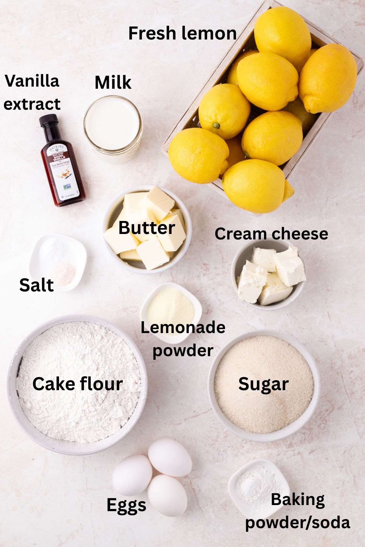 Ingredients to make a lemon sheet cake on a surface with labels to identify each one.