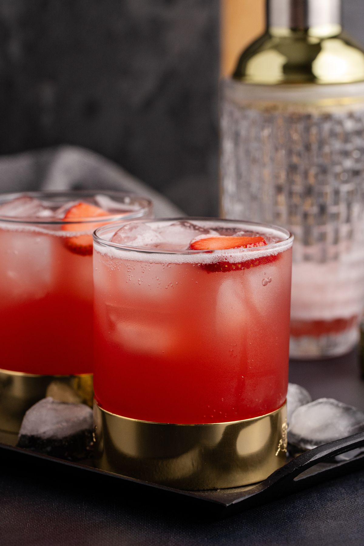 Two drinks and cocktail shaker on table.