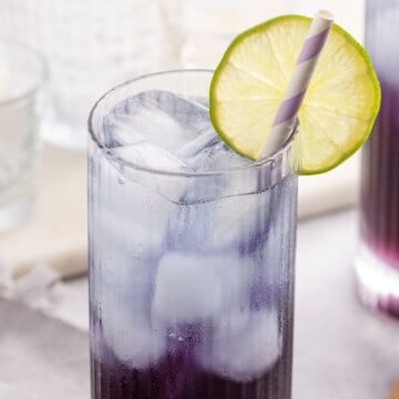 Purple Rain Cocktail recipe in a glass served with a straw and garnished with a lime slice.