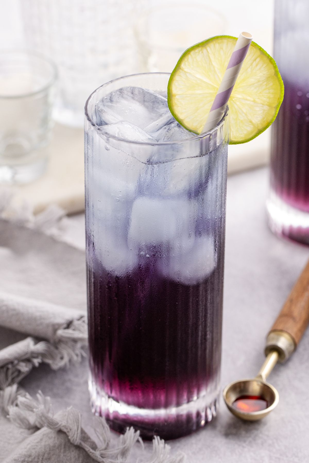 A Cocktail in a glass served with a straw and garnished with a lime slice on a table.