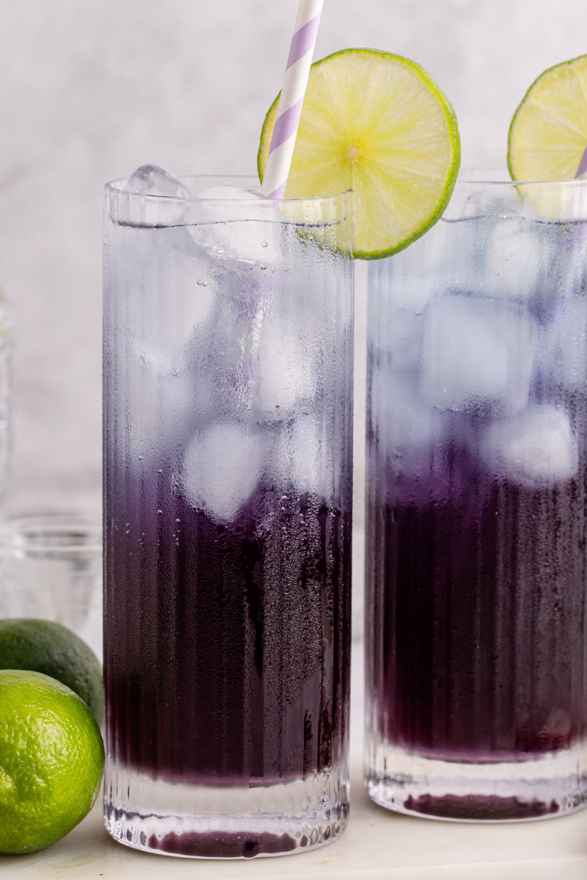 A cocktail in a glass served with a straw and garnished with a lime slice on table.