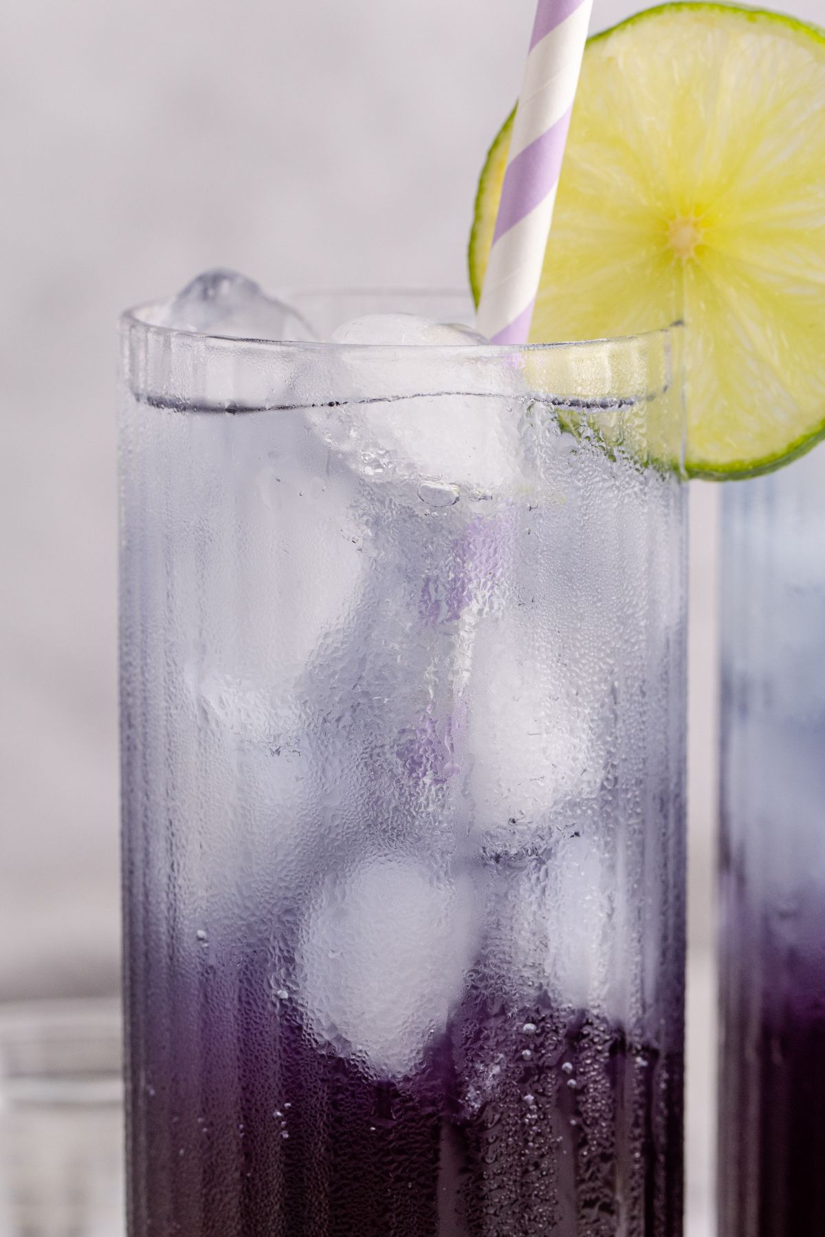 Two cocktails in a glass served with a straw and garnished with a lime slice.