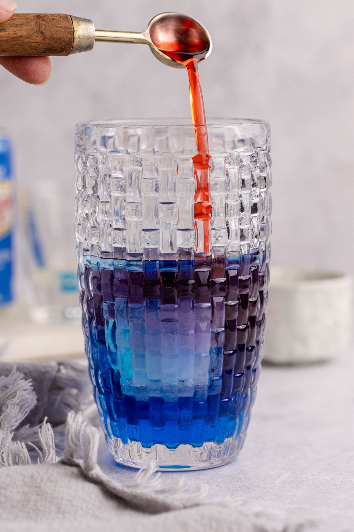 Cocktail shaker with ice, vodka, blue curacao, cranberry juice and grenadine being added.