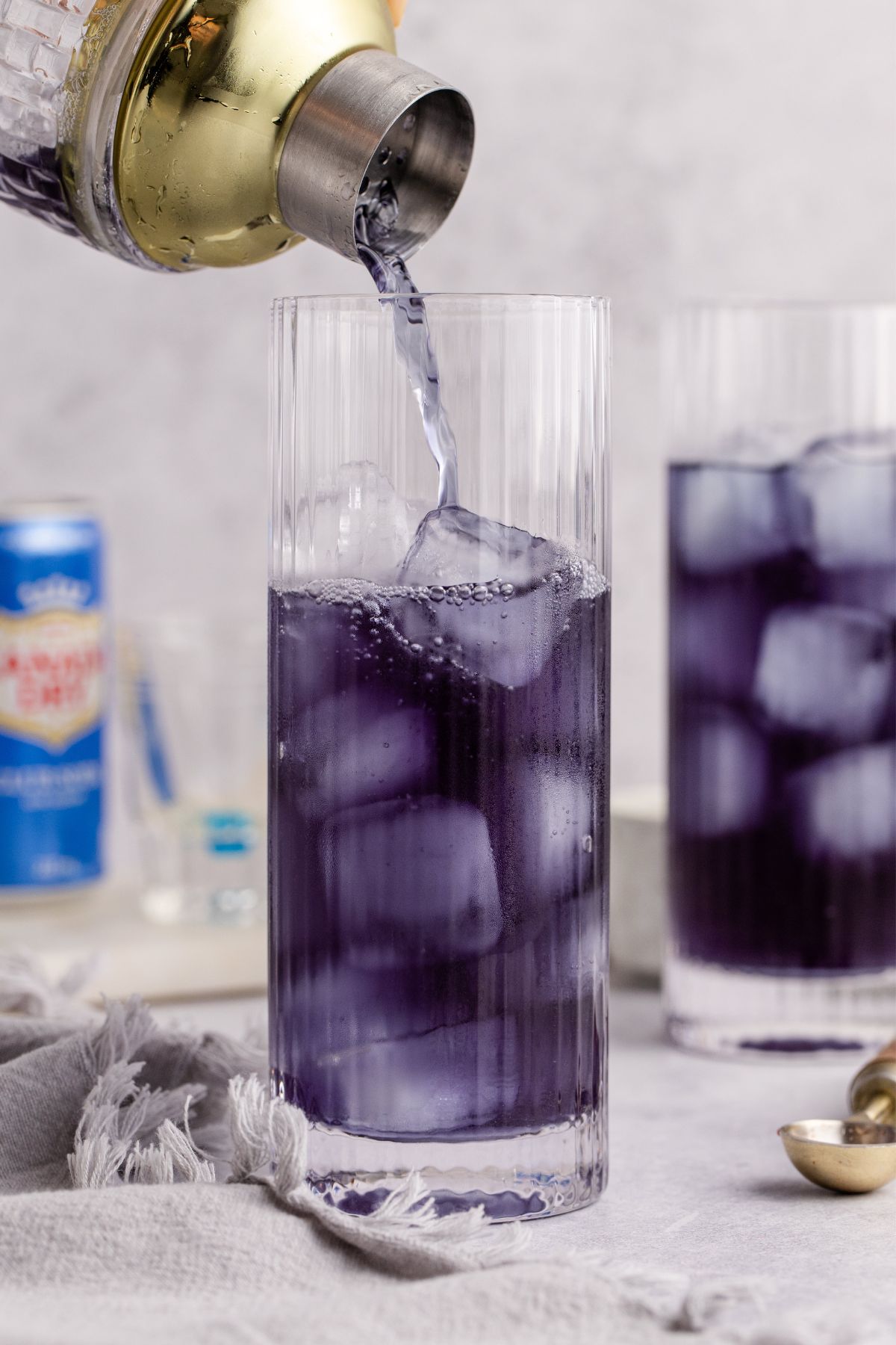 Shaken cocktail being added to ice filled tall glass.