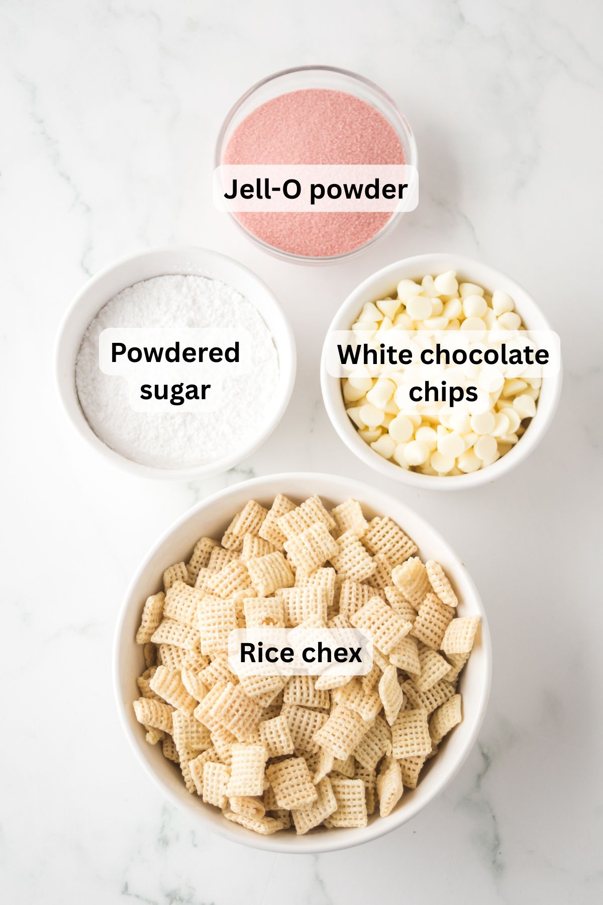 The ingredients needed to make strawberry Chex mix in bowls on the table with labels to identify each one.