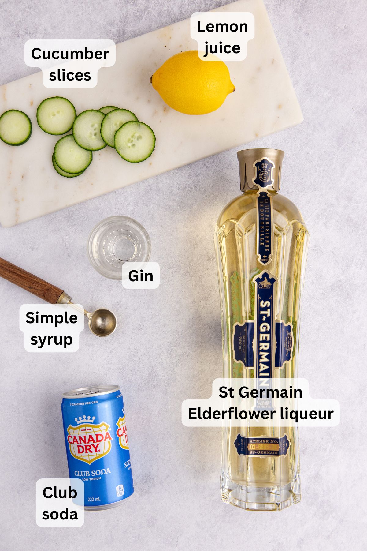 The ingredients needed to make a white linen cocktail on the table with labels to identify each one.