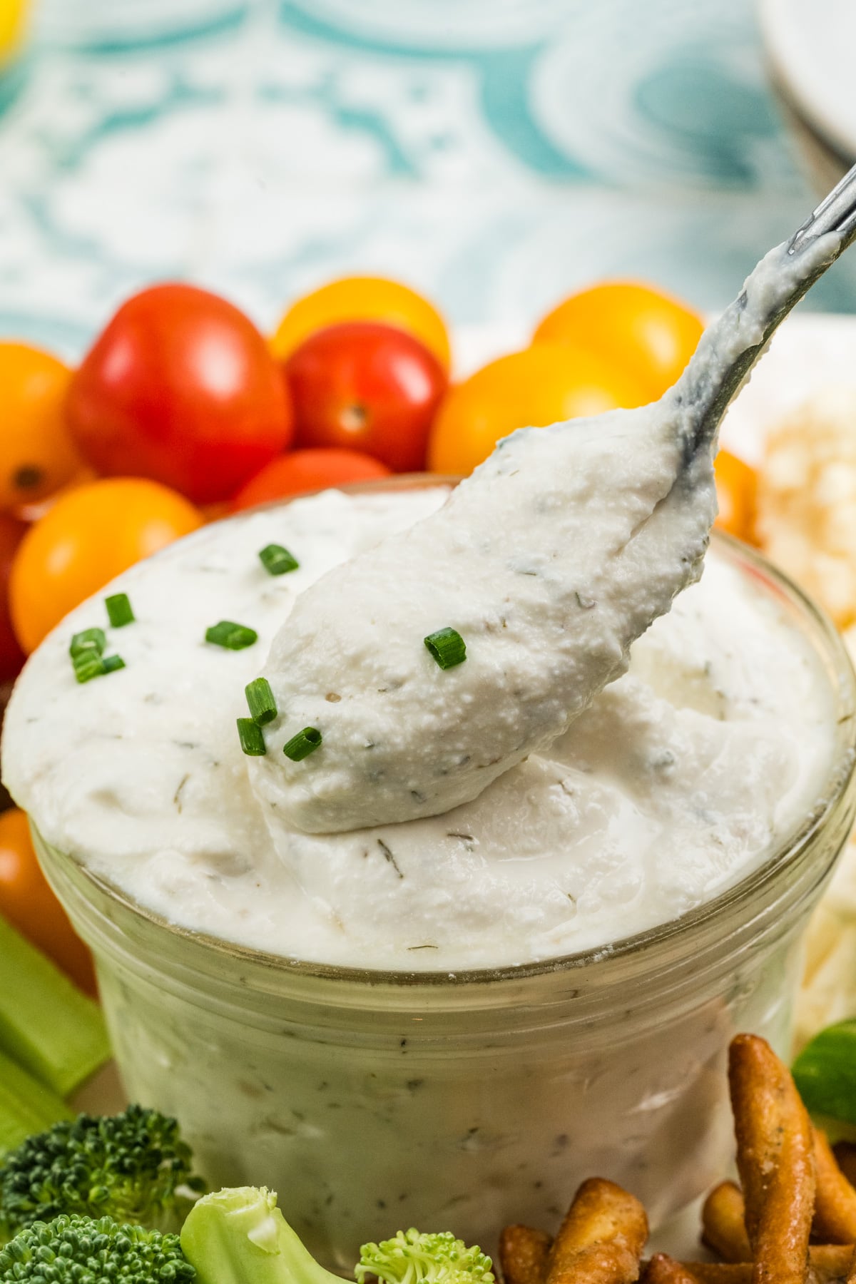 A spoon lifting out of a bowl of dip on a platter full of vegetables.