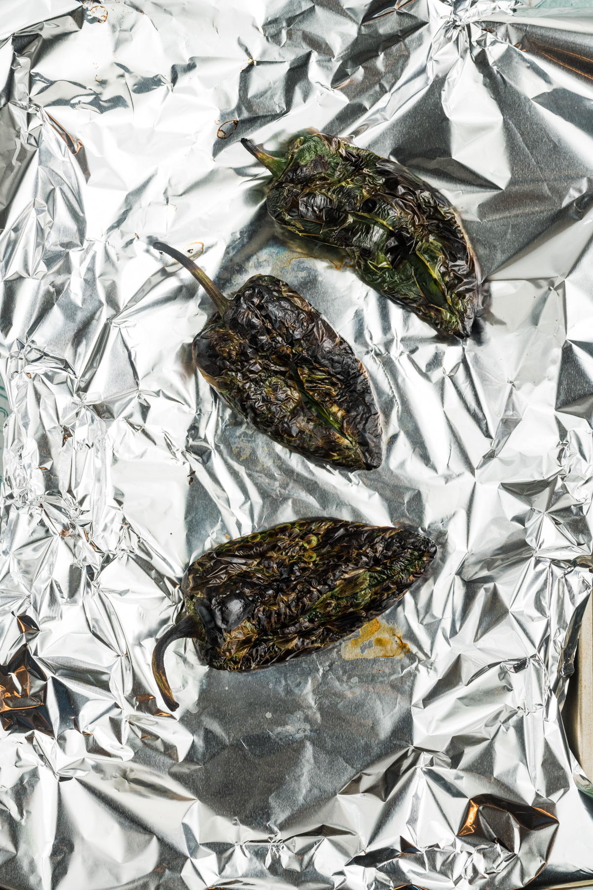 Charred peppers on a foil lined pan.