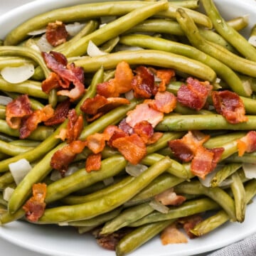 A plate full of cooked green beans and lbacon.