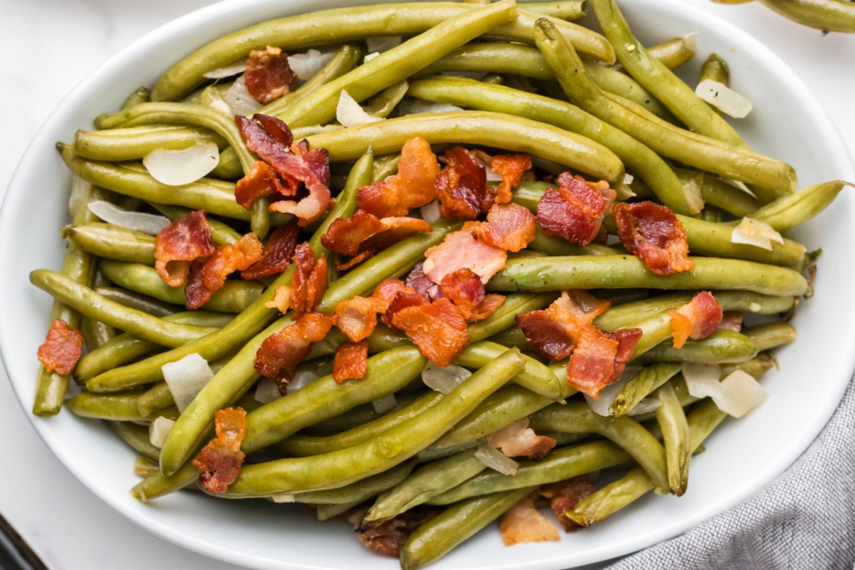 A plate full of cooked green beans and lbacon.