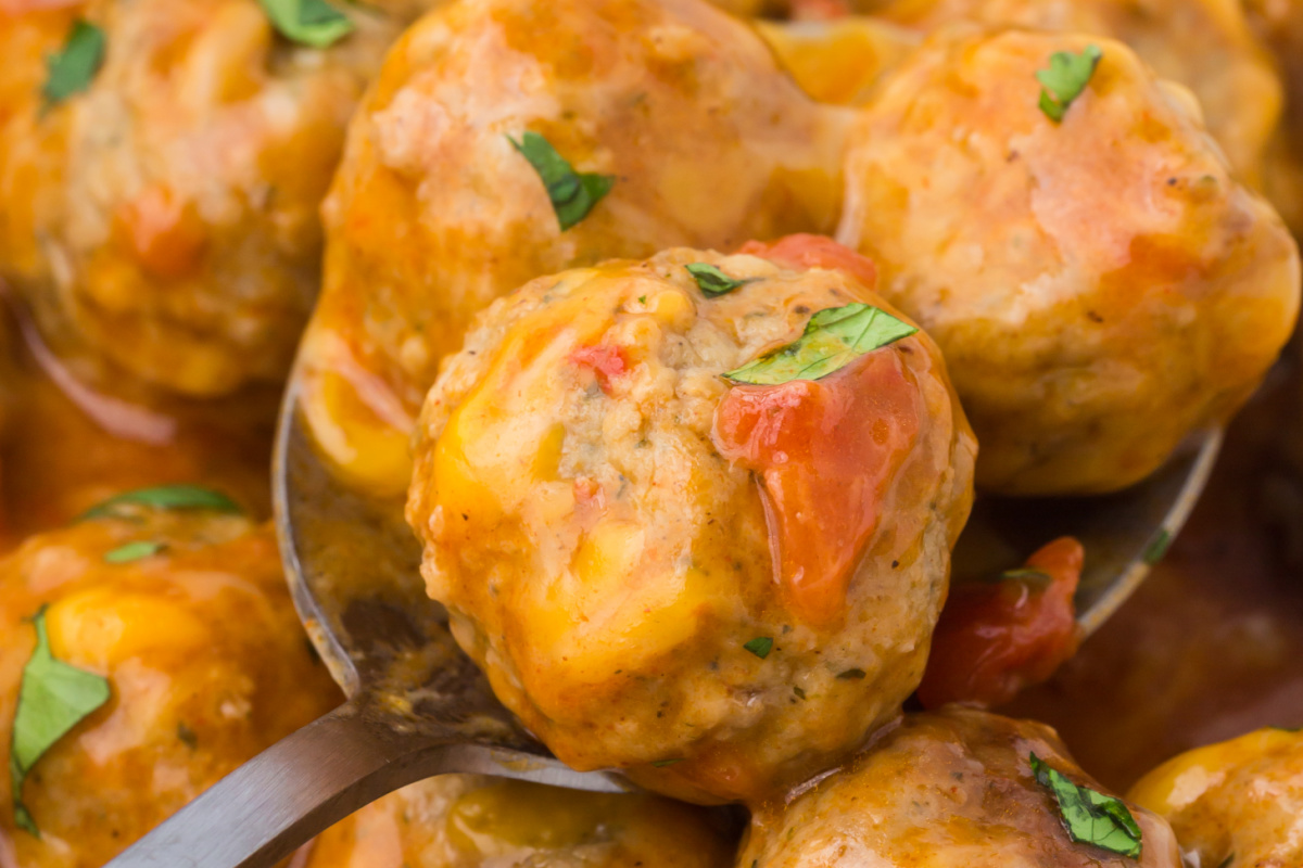 A spoon in a bowl full of meatballs.