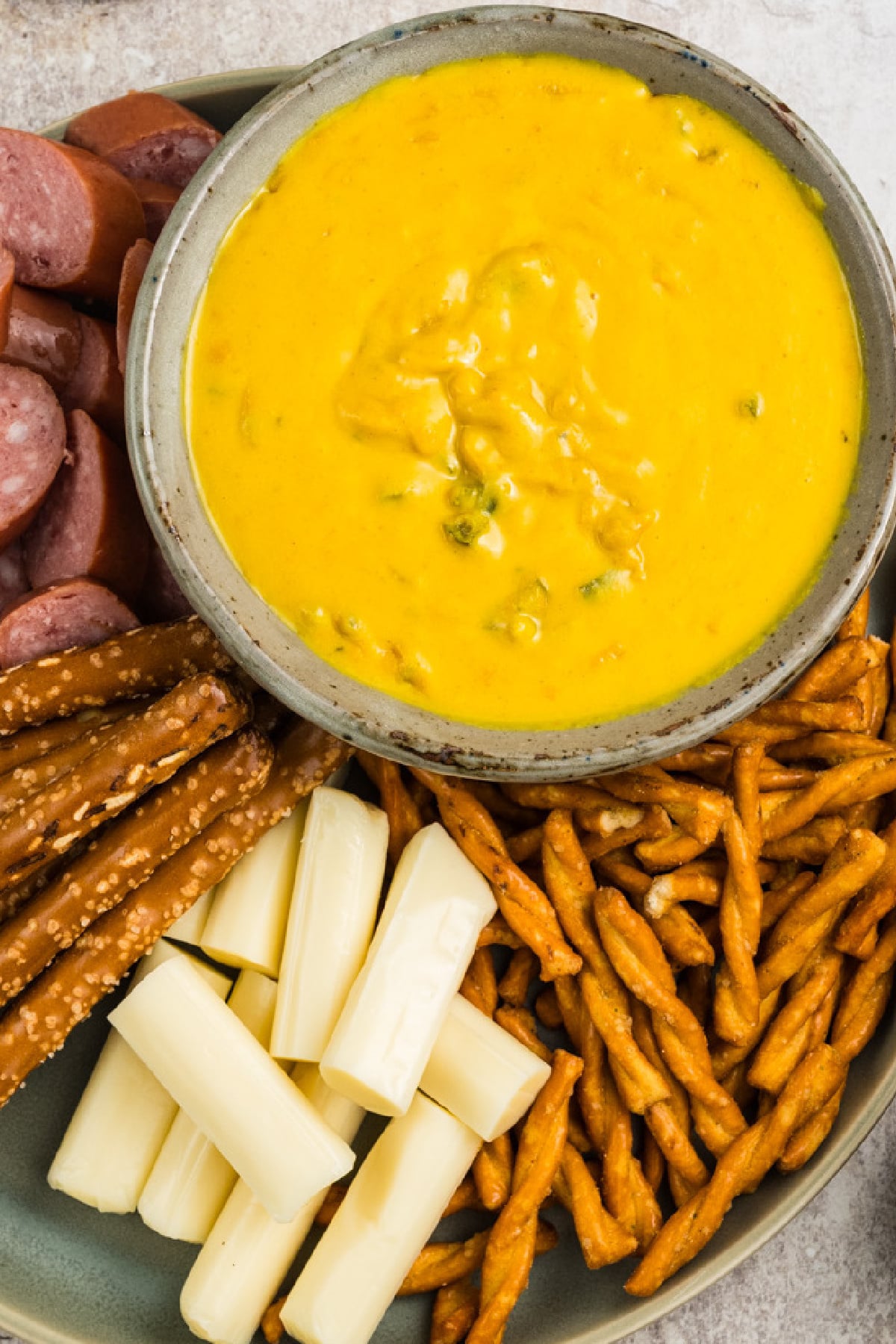 A bowl of mustard on a platter with pretzels, salami and cheese.