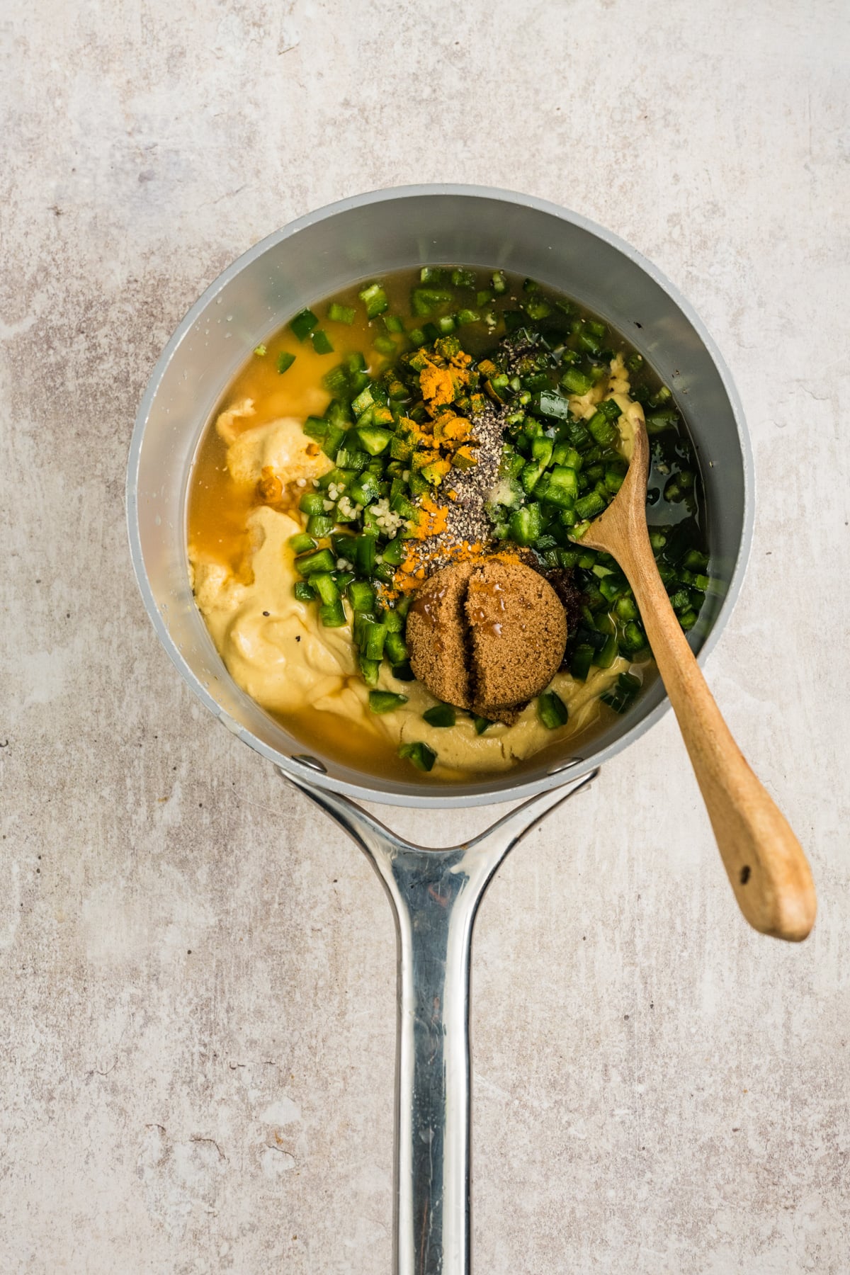 All of the ingredients in a saucepan ready to simmer with a wooden spoon.