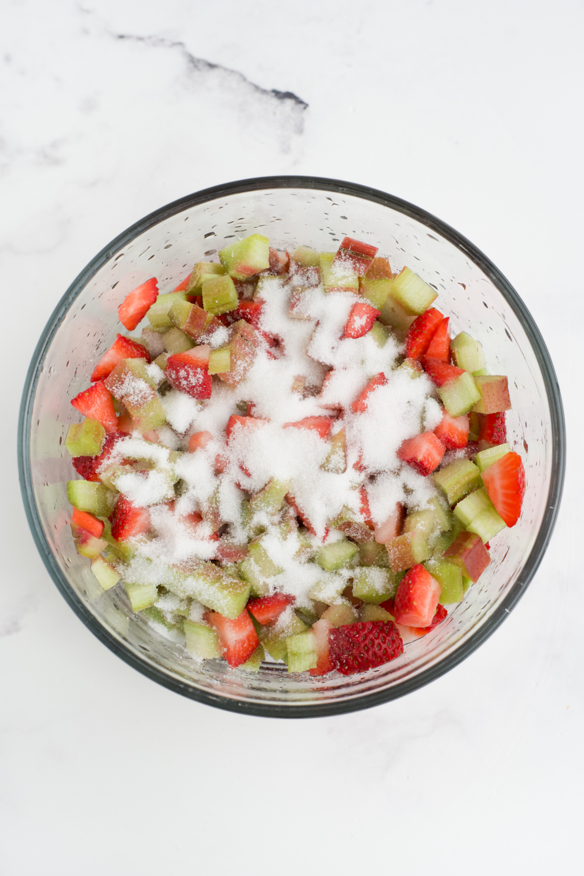 Rhubarb and strawberries in sugar in a bowl.