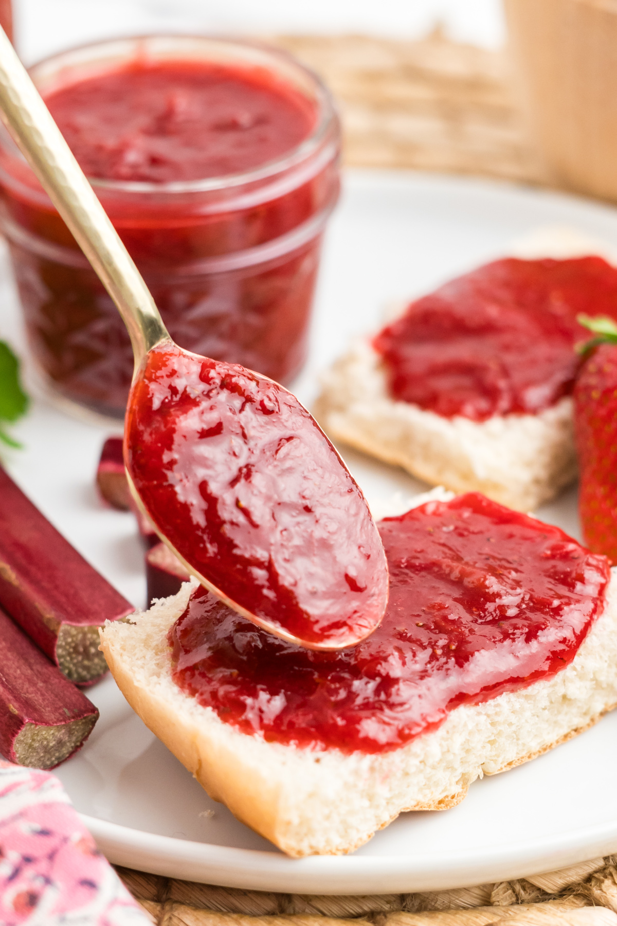 A spoon adding some rhubarb and strawberry preserves onto bread.