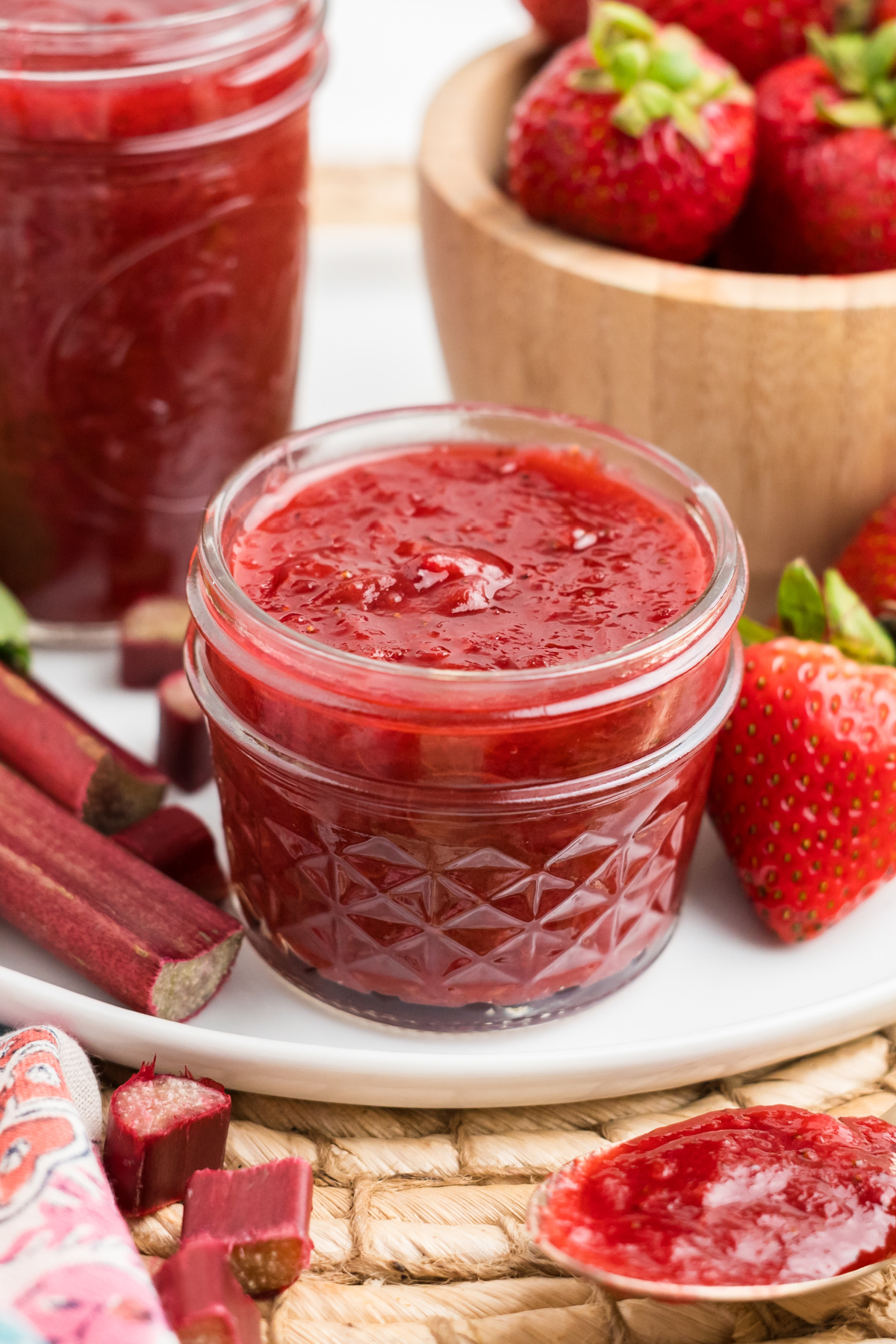A jar of strawberry preserves next to a strawberry and rhubarb.