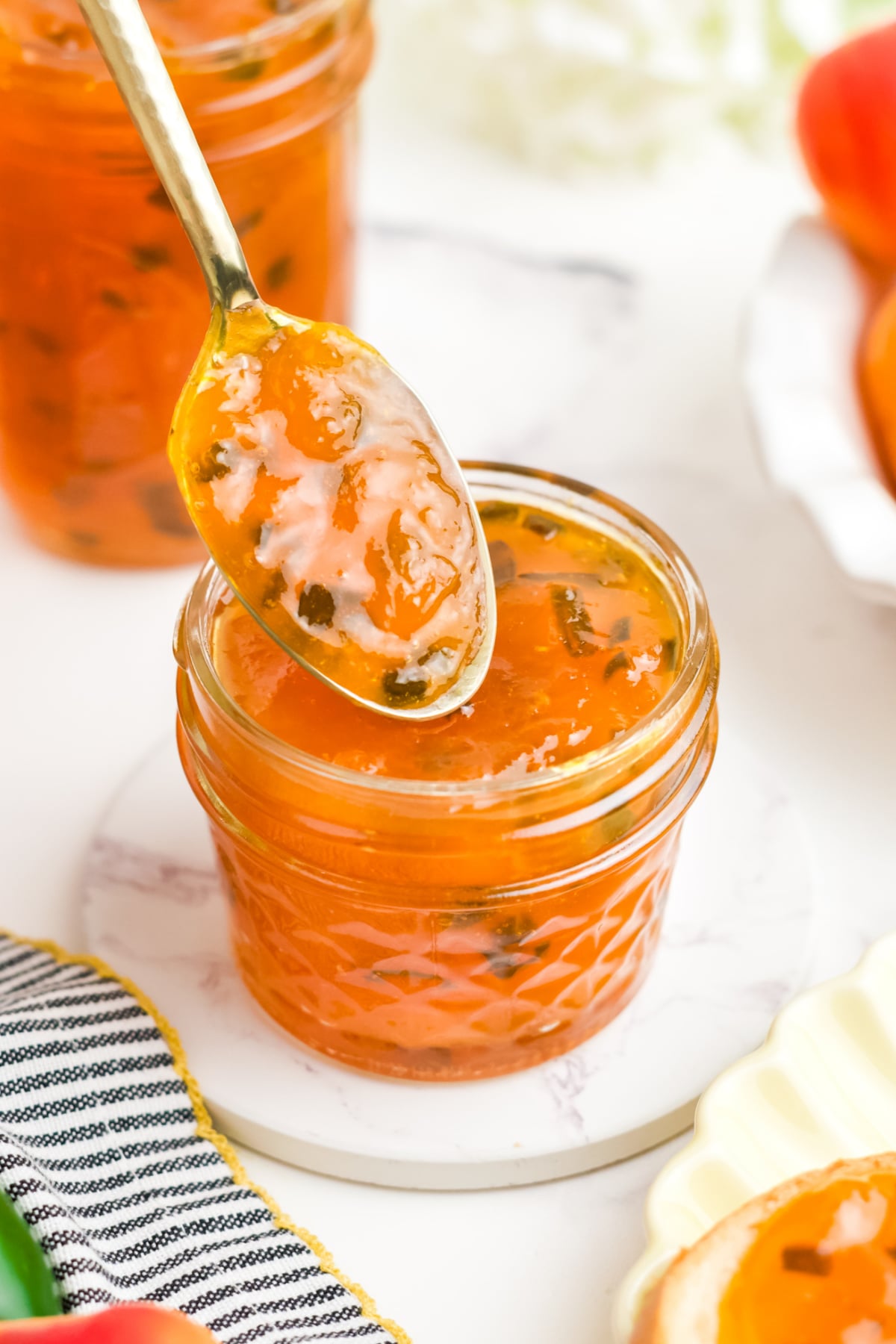 Apricot jam on a mason jar with a a spoonful held up over the jar.