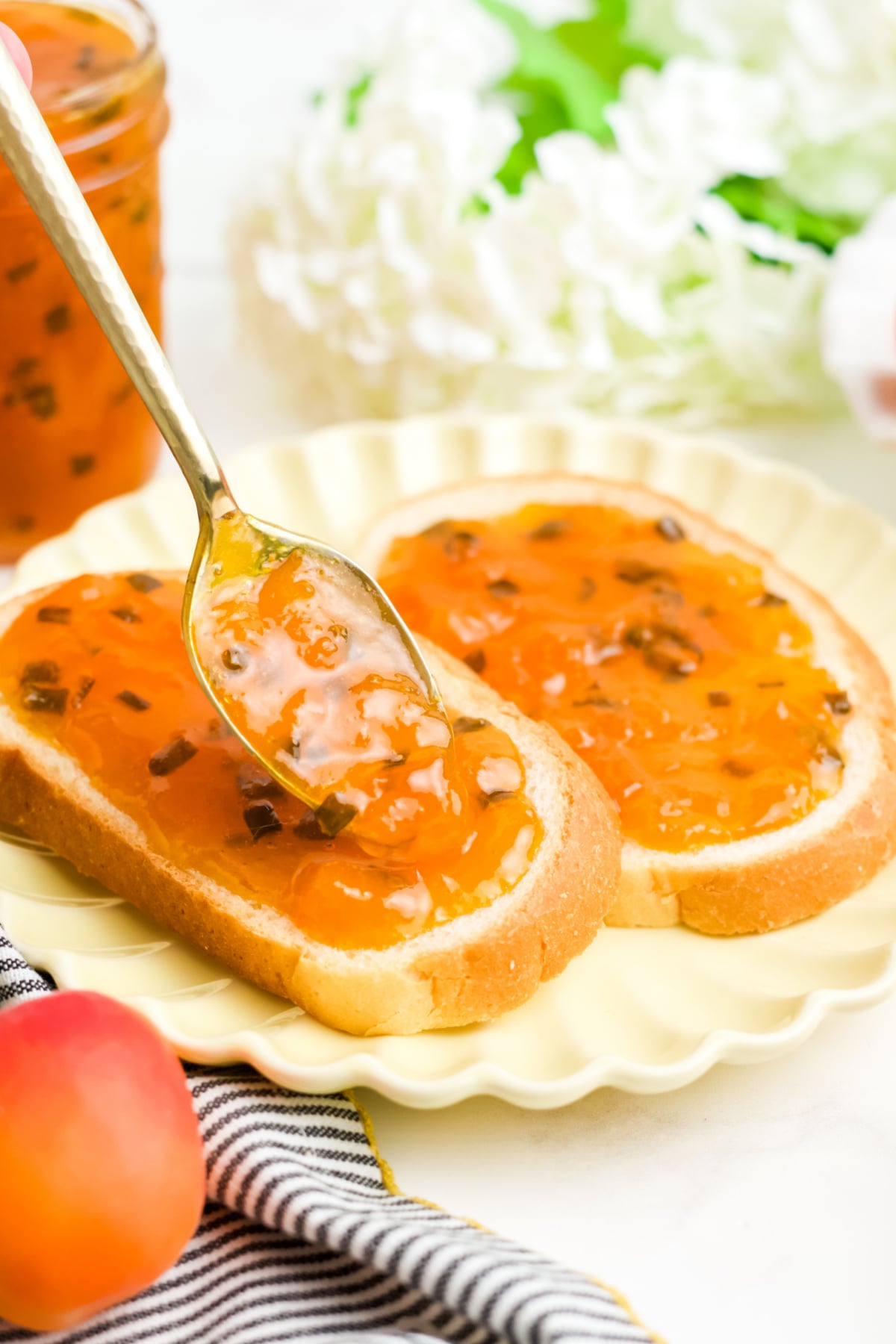 A spoon spreading some apricot jalapeno jam on slices of bread.