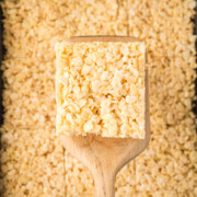 A square on a spatula held above a pan full of browned butter Rice Krispie treats