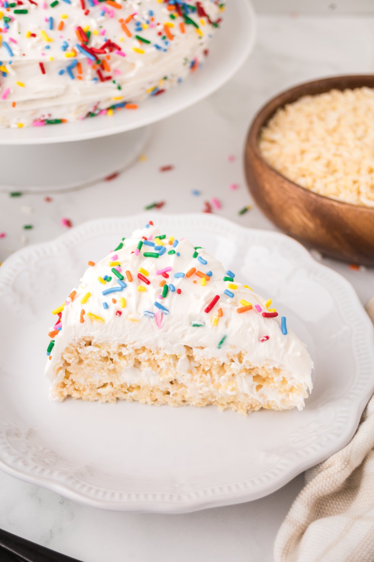 A slice of cake rice krispie treats with vanilla frosting and rainbow sprinkles