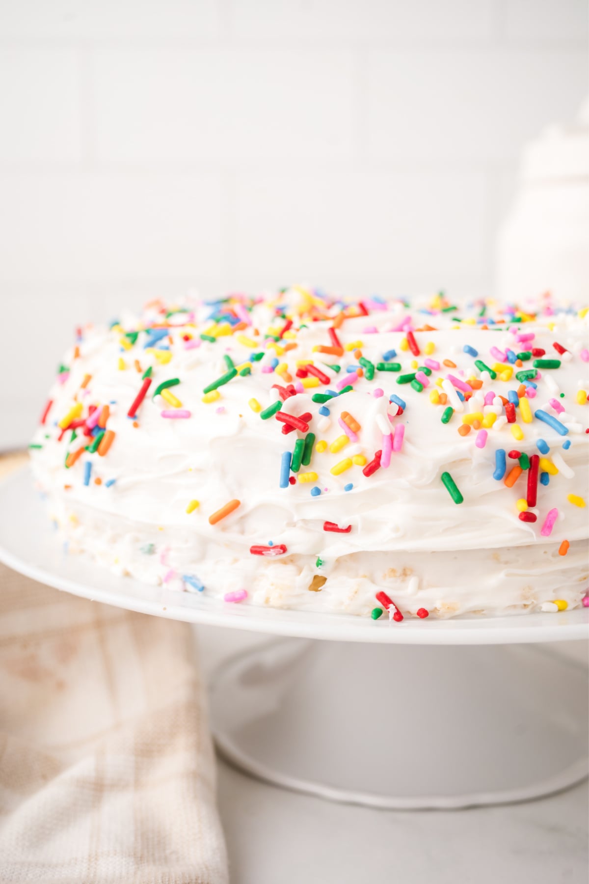 A frosted layer cake on a platter covered in sprinkles.