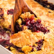 A wooden spoon scooping up a serving of blackberry dump cake.