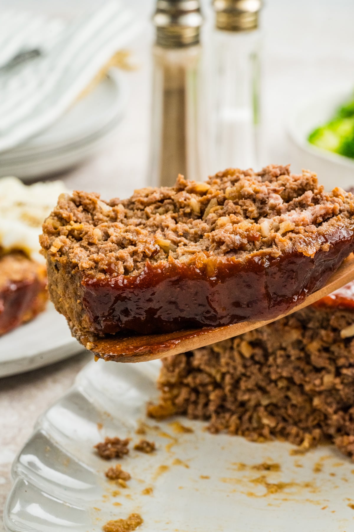 A slice of meatloaf lifted on a wooden spoon.