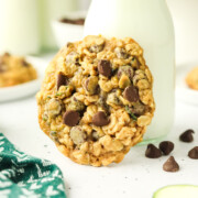 A zucchini chocolate chip cookie leaning on a jar of milk.