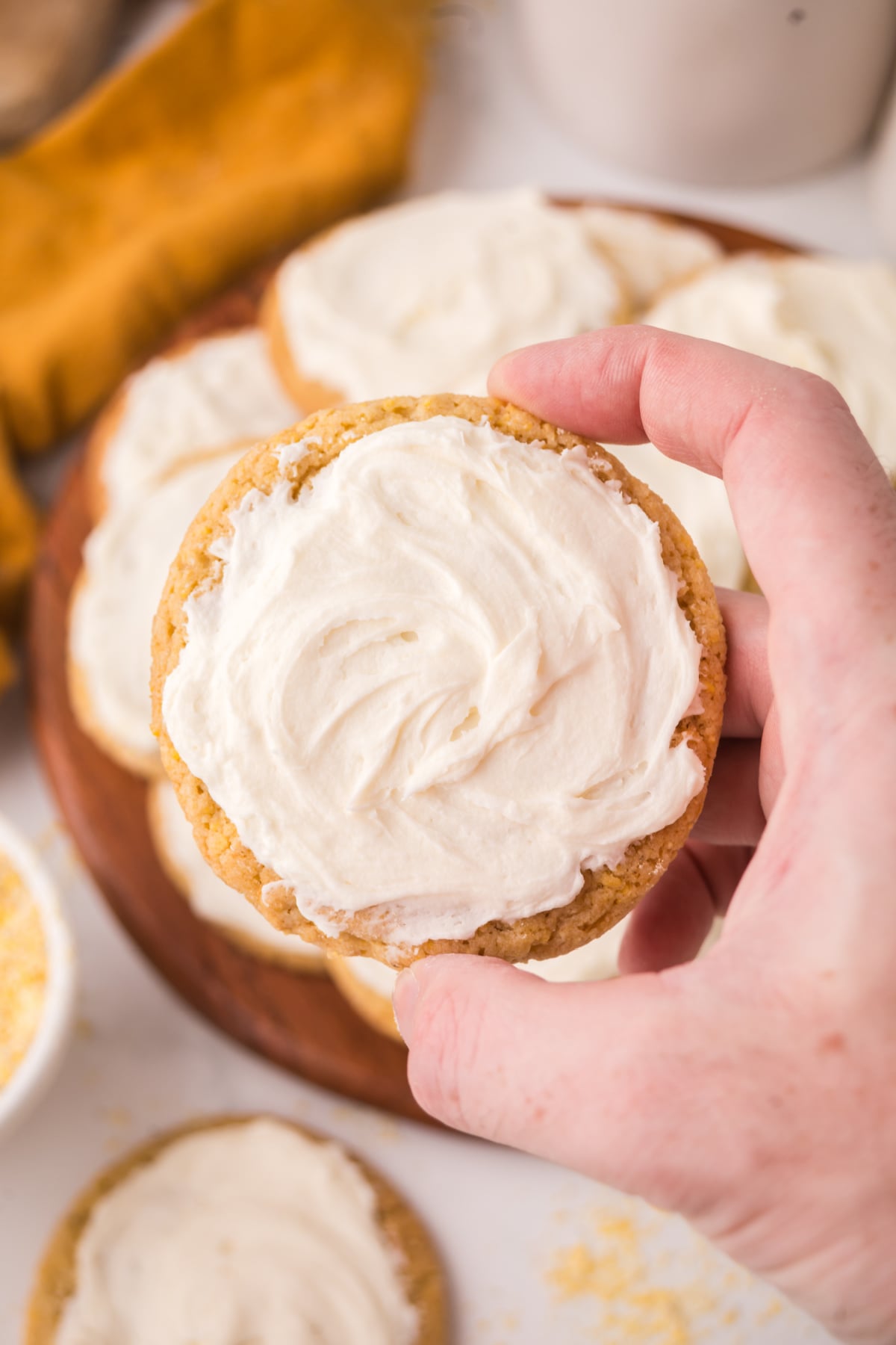 A hand holding up a cornbread cookie with frosting on top.