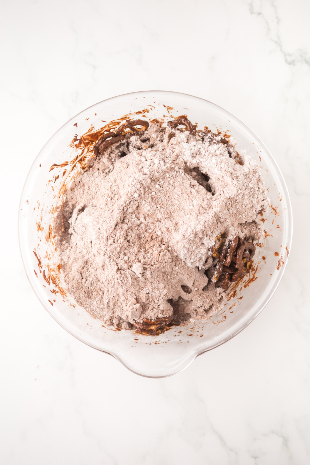 Chocolate covered pretzels in bowl covered with powdered sugar, brownie mix and salt.