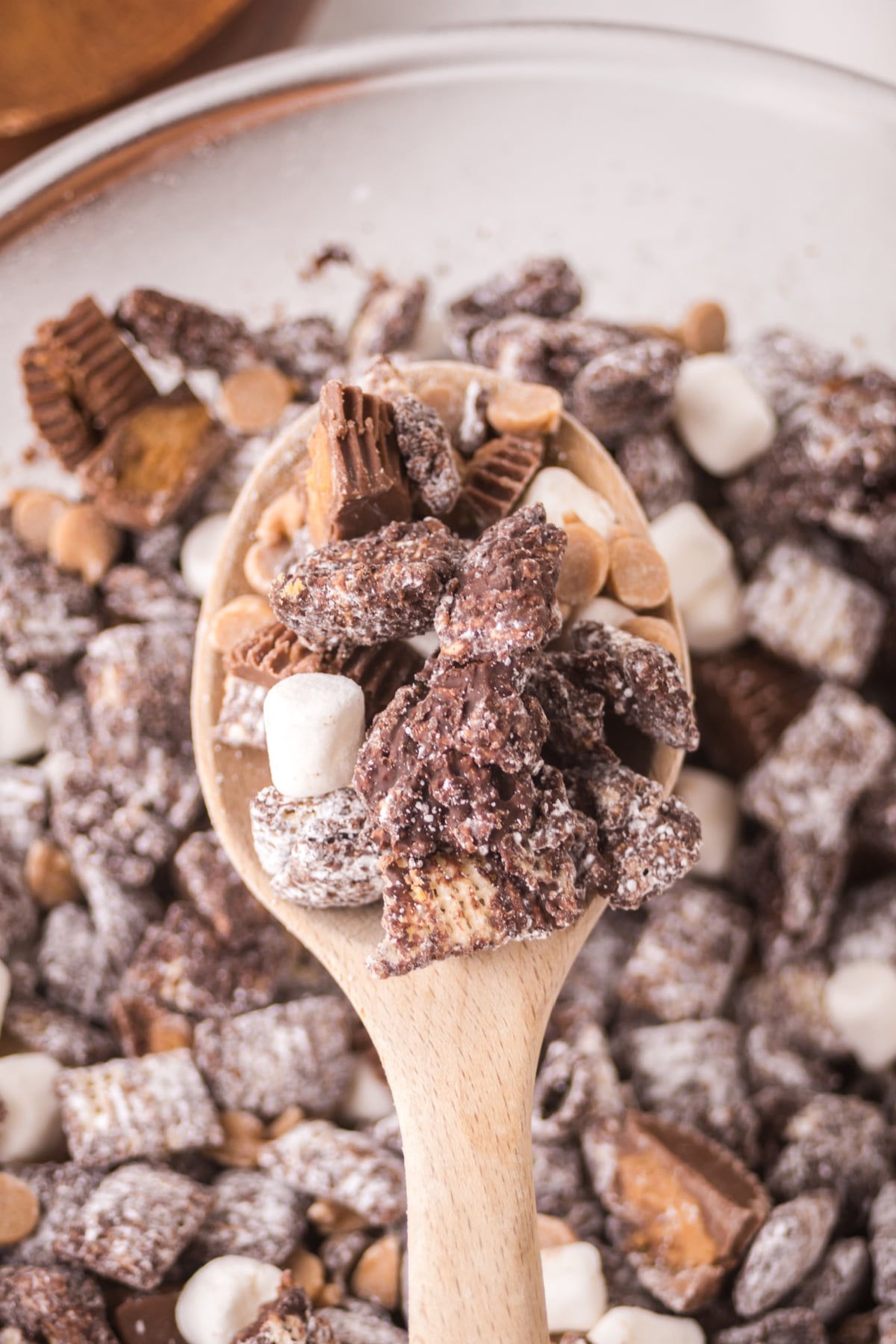 A wooden spoonful of muddy buddies over a bowlful 