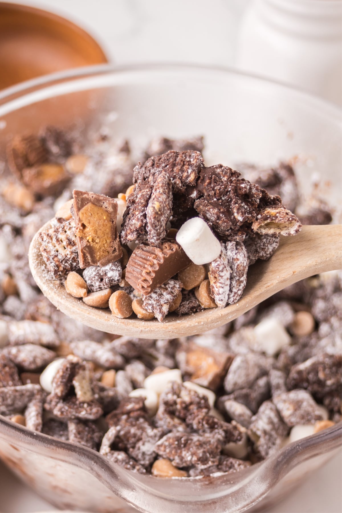 A big wooden spoonful of muddy buddies over a bowlful 