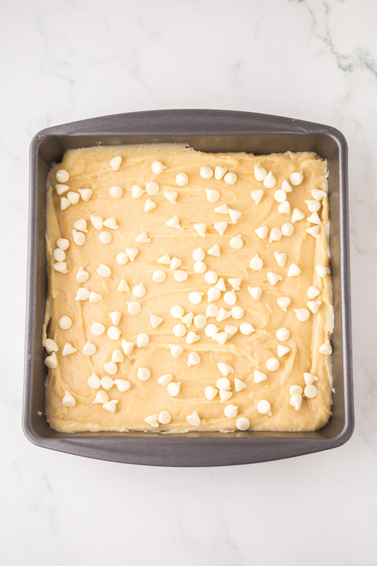 White chocolate brownie batter poured into the baking pan and topped with chips. 